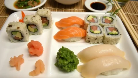 A beautifully arranged platter of sushi rolls, including California rolls, nigiri, and sashimi, garnished with pickled ginger, wasabi, and soy sauce, set on a bamboo mat with chopsticks and green tea.